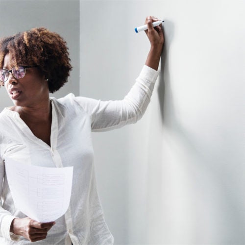 a woman stands at a whiteboard and looks behind her