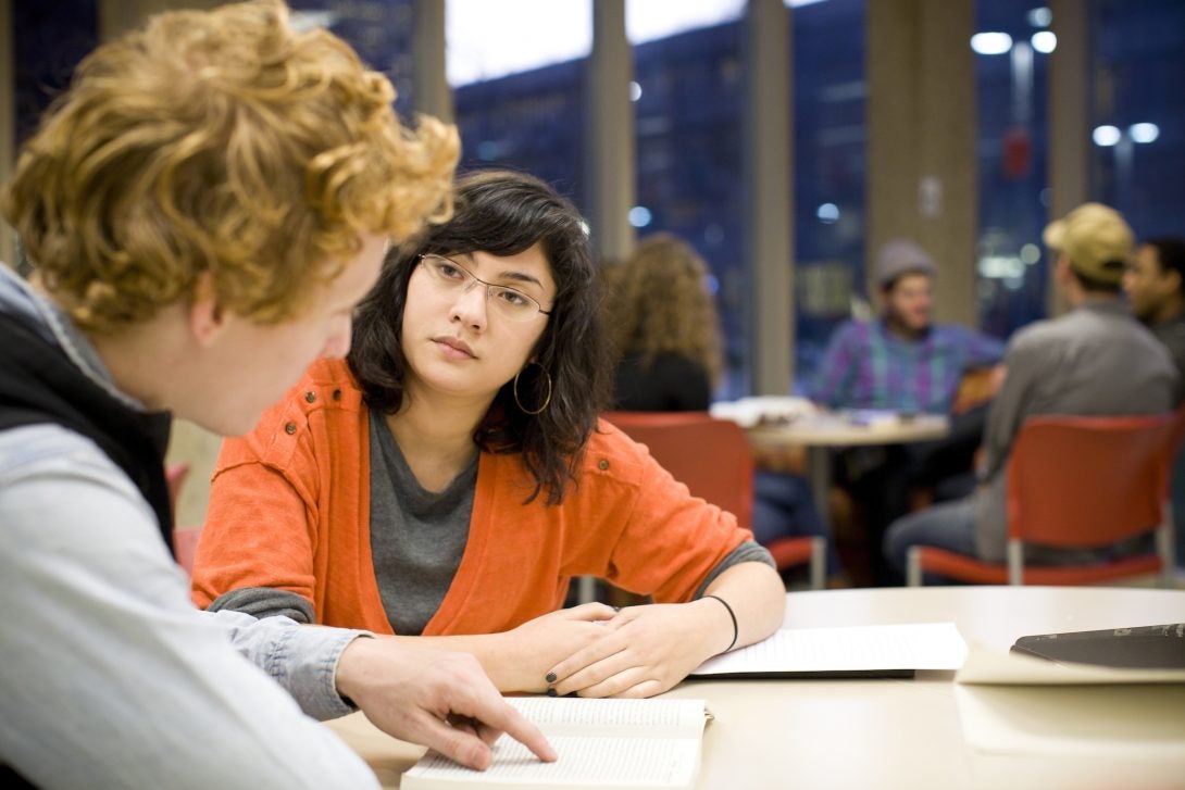 students study at a library table, books in front of them