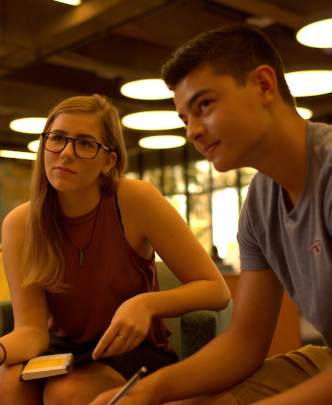 A woman and a man listen attentively to a speaker as they take down notes on a notebook.